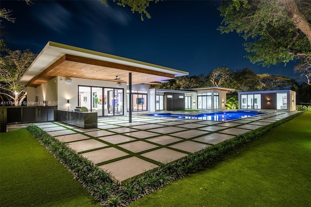 back of house at twilight with a patio, an outdoor pool, and stucco siding