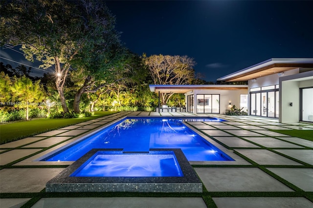 pool at night with a patio and a pool with connected hot tub