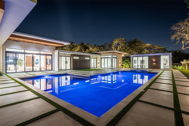 pool at twilight with an outdoor pool, a patio area, and an in-ground hot tub