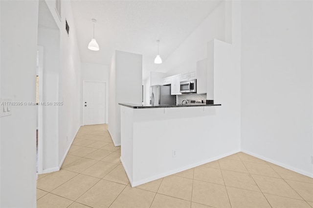kitchen featuring light tile patterned floors, dark countertops, decorative light fixtures, appliances with stainless steel finishes, and high vaulted ceiling