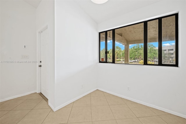 empty room featuring light tile patterned floors, baseboards, and vaulted ceiling
