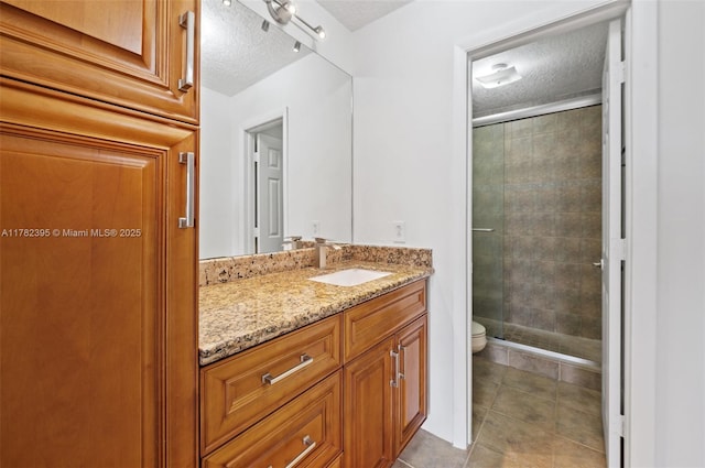 bathroom featuring toilet, a textured ceiling, tile patterned flooring, vanity, and a stall shower