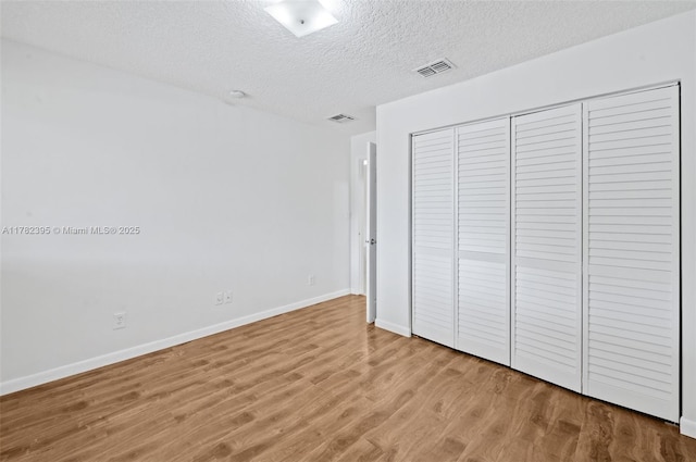unfurnished bedroom with visible vents, baseboards, wood finished floors, and a textured ceiling