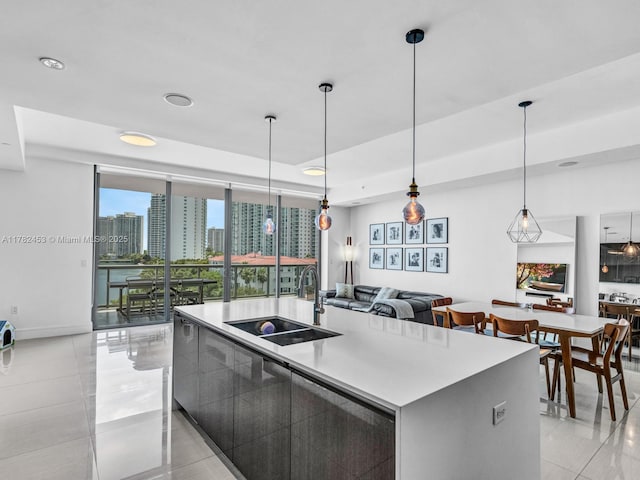 kitchen with decorative light fixtures, modern cabinets, a sink, light countertops, and an island with sink