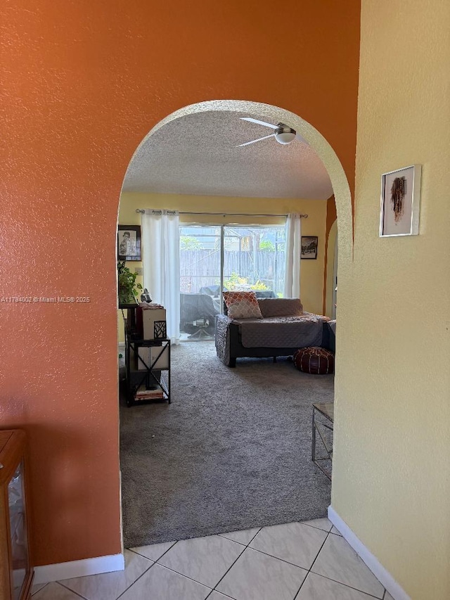 hallway featuring baseboards, arched walkways, a textured wall, carpet floors, and tile patterned flooring