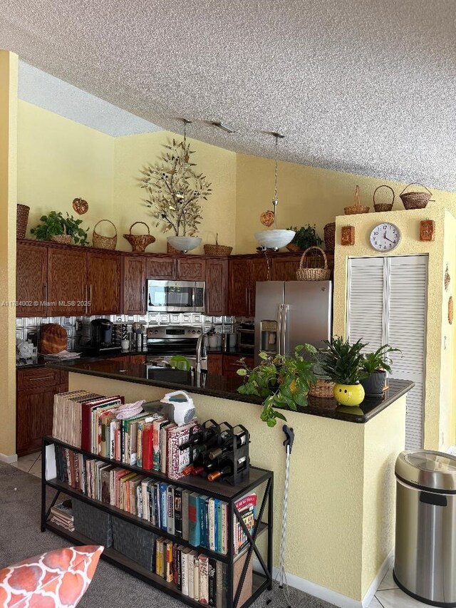 kitchen with a kitchen bar, a textured ceiling, appliances with stainless steel finishes, and dark countertops