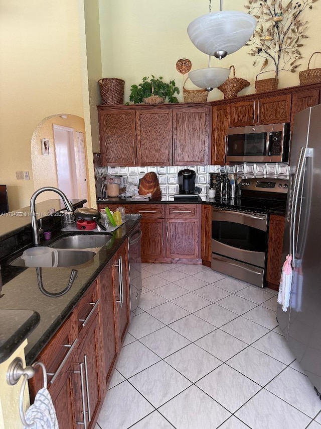kitchen with a sink, light tile patterned floors, appliances with stainless steel finishes, and dark stone counters