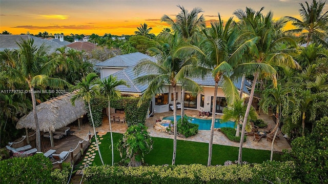 pool at dusk featuring a patio area, an outdoor pool, and a lawn