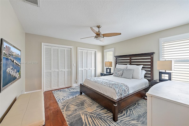 bedroom with baseboards, a textured ceiling, two closets, visible vents, and wood finished floors