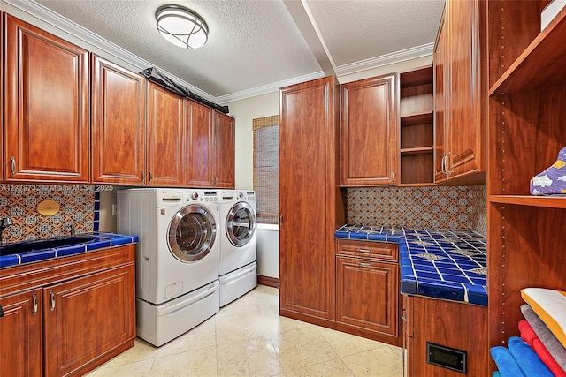 washroom with washing machine and dryer, a textured ceiling, ornamental molding, and cabinet space