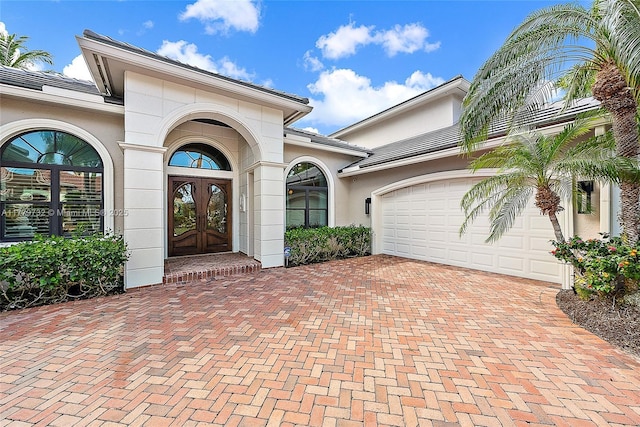 doorway to property featuring a garage, a tile roof, stucco siding, french doors, and decorative driveway
