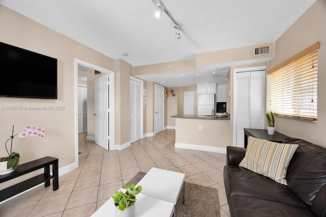 living room with a textured ceiling, rail lighting, baseboards, light tile patterned floors, and visible vents