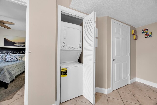 clothes washing area featuring laundry area, baseboards, stacked washing maching and dryer, and light tile patterned floors