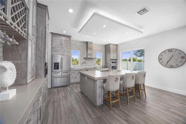 kitchen with a kitchen breakfast bar, a sink, stainless steel appliances, wall chimney exhaust hood, and visible vents