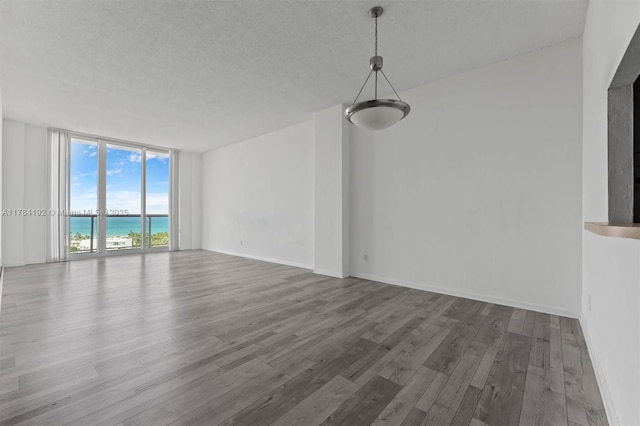 spare room with a water view, a wall of windows, a textured ceiling, and wood finished floors