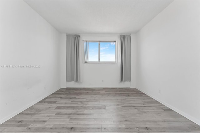 unfurnished room featuring light wood-type flooring, baseboards, and a textured ceiling