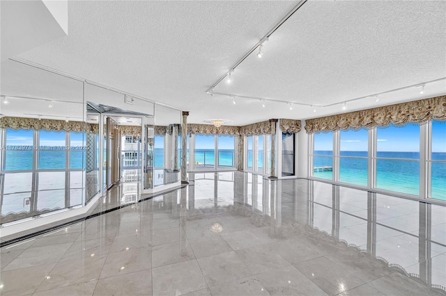 empty room featuring a water view, a textured ceiling, and tile patterned flooring