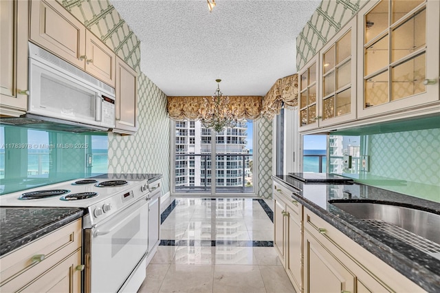 kitchen featuring cream cabinets, wallpapered walls, white appliances, and a notable chandelier