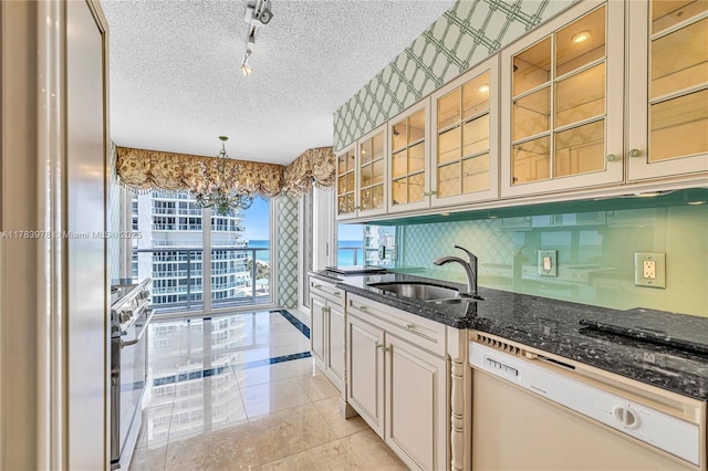 kitchen with a textured ceiling, white dishwasher, rail lighting, a sink, and a notable chandelier