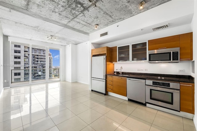 kitchen with brown cabinetry, dark countertops, a sink, and stainless steel appliances
