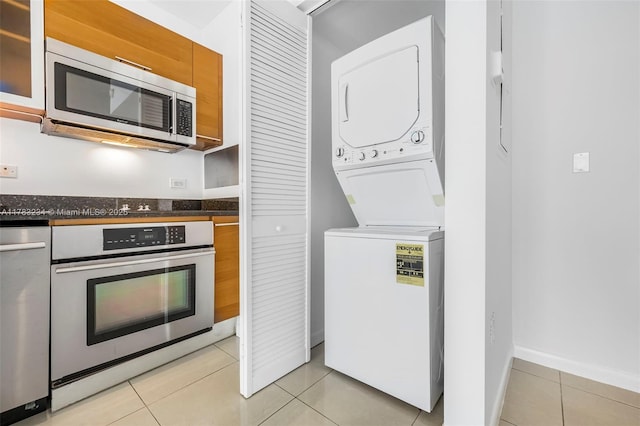 3470 E Coast Ave Unit H2706, Miami, FL 33137 - kitchen featuring stainless steel appliances, stacked washing machine and dryer, dark countertops, light tile patterned flooring, and brown cabinets