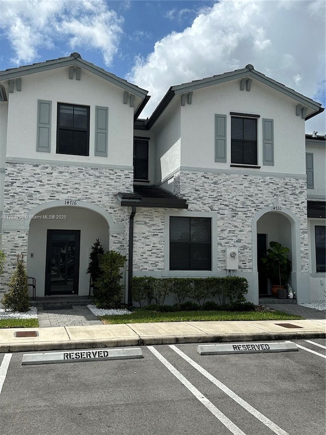 view of front of house featuring uncovered parking, stucco siding, and stone siding