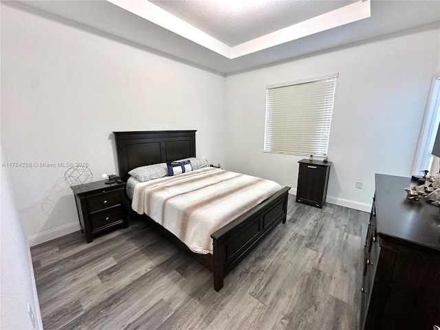 bedroom with a raised ceiling, baseboards, and wood finished floors