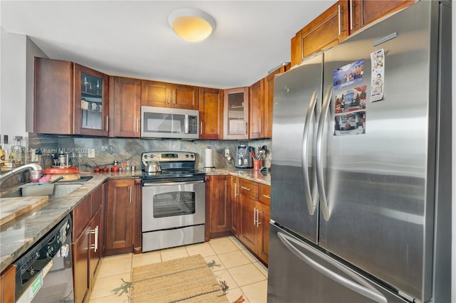 kitchen featuring light tile patterned floors, a sink, light stone countertops, decorative backsplash, and stainless steel appliances