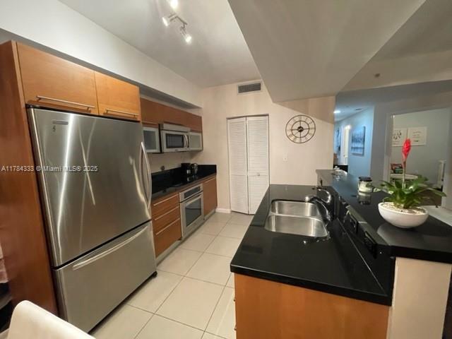 kitchen with light tile patterned floors, dark countertops, brown cabinets, stainless steel appliances, and a sink