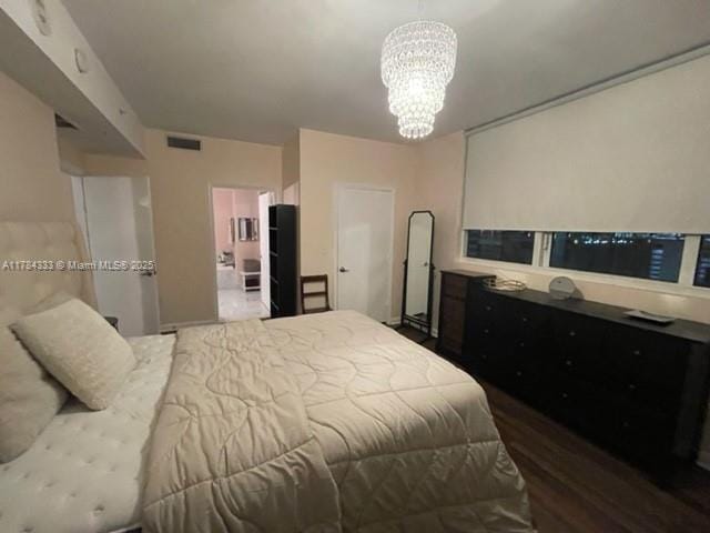 bedroom featuring wood finished floors, a notable chandelier, visible vents, and connected bathroom