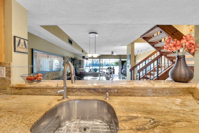 kitchen featuring a textured ceiling, visible vents, light stone counters, a sink, and decorative light fixtures