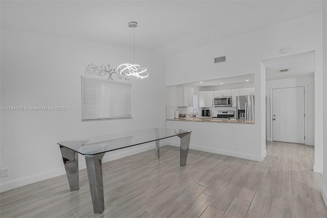 interior space featuring light wood-type flooring, vaulted ceiling, an inviting chandelier, visible vents, and a sink