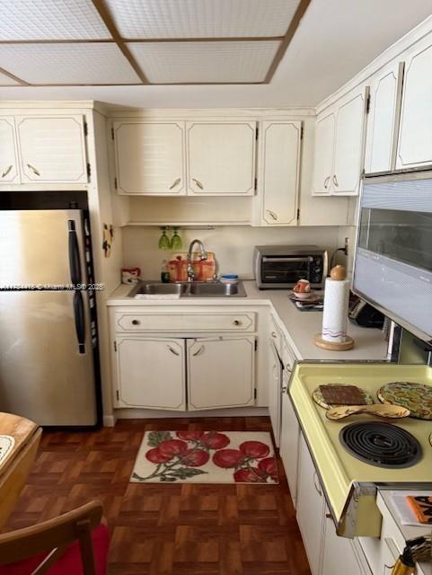 kitchen with a toaster, white microwave, light countertops, freestanding refrigerator, and a sink