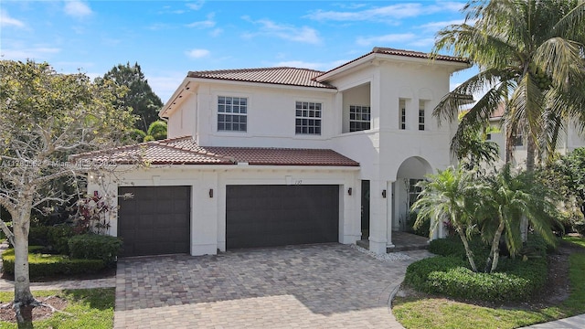 mediterranean / spanish home with a tiled roof, a garage, stucco siding, and decorative driveway