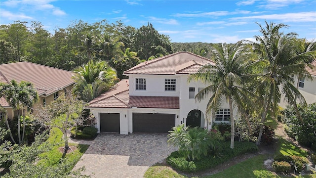 mediterranean / spanish home with a tile roof, a garage, decorative driveway, and stucco siding
