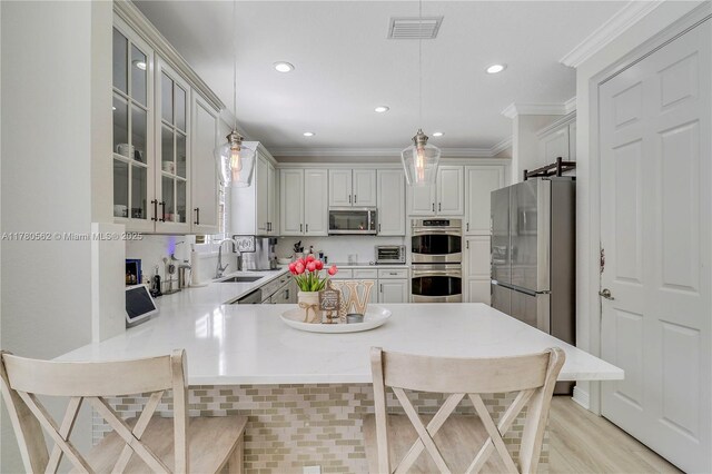 kitchen with visible vents, a sink, a peninsula, crown molding, and stainless steel appliances