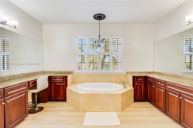 full bathroom with a chandelier, vanity, a garden tub, and wood finished floors