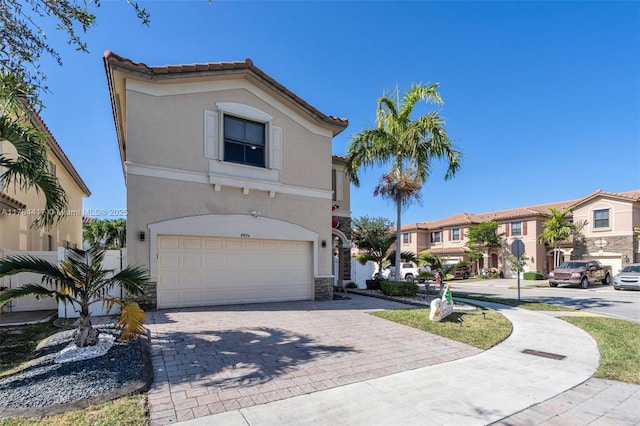 mediterranean / spanish-style home featuring a residential view, stucco siding, stone siding, decorative driveway, and an attached garage