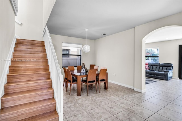 dining room with light tile patterned floors, baseboards, visible vents, arched walkways, and stairway