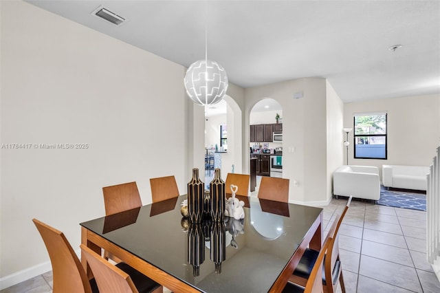 dining area featuring arched walkways, light tile patterned floors, baseboards, and visible vents