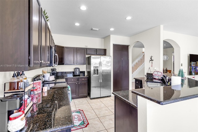 kitchen with arched walkways, dark brown cabinets, dark stone countertops, a sink, and stainless steel appliances