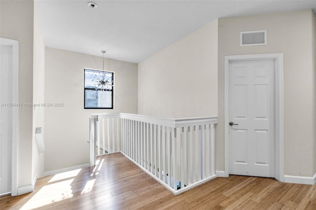 hall with visible vents, baseboards, an inviting chandelier, an upstairs landing, and wood-type flooring