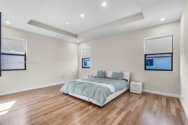 bedroom with a raised ceiling, light wood-style floors, and baseboards