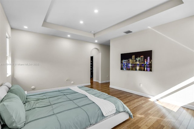 bedroom featuring baseboards, recessed lighting, a raised ceiling, arched walkways, and wood finished floors