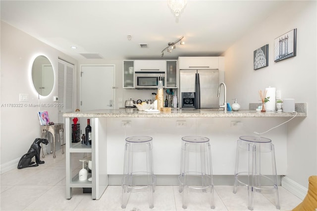 kitchen featuring a kitchen bar, a peninsula, appliances with stainless steel finishes, and visible vents