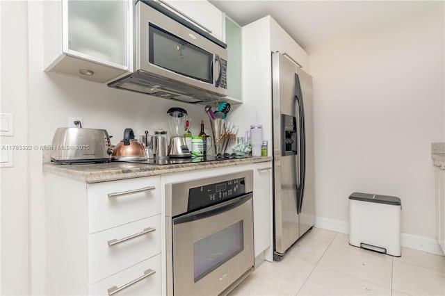 kitchen with baseboards, light tile patterned floors, white cabinets, light stone countertops, and appliances with stainless steel finishes
