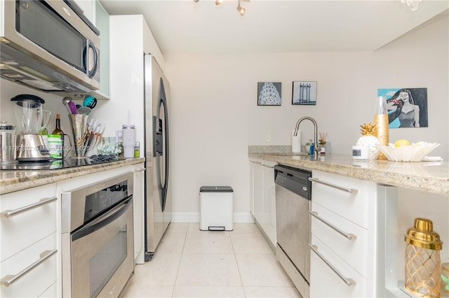 kitchen featuring light tile patterned floors, a sink, appliances with stainless steel finishes, a peninsula, and white cabinetry
