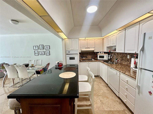 kitchen featuring white appliances, a center island, under cabinet range hood, a sink, and decorative backsplash