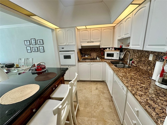 kitchen with white appliances, under cabinet range hood, a sink, lofted ceiling, and backsplash