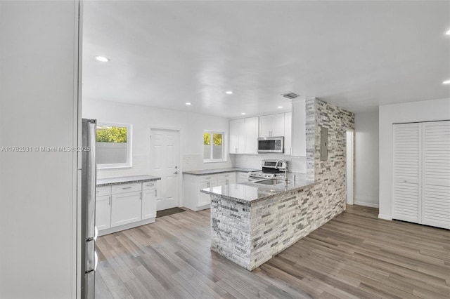 kitchen featuring appliances with stainless steel finishes, light wood-style floors, a peninsula, white cabinetry, and light stone countertops